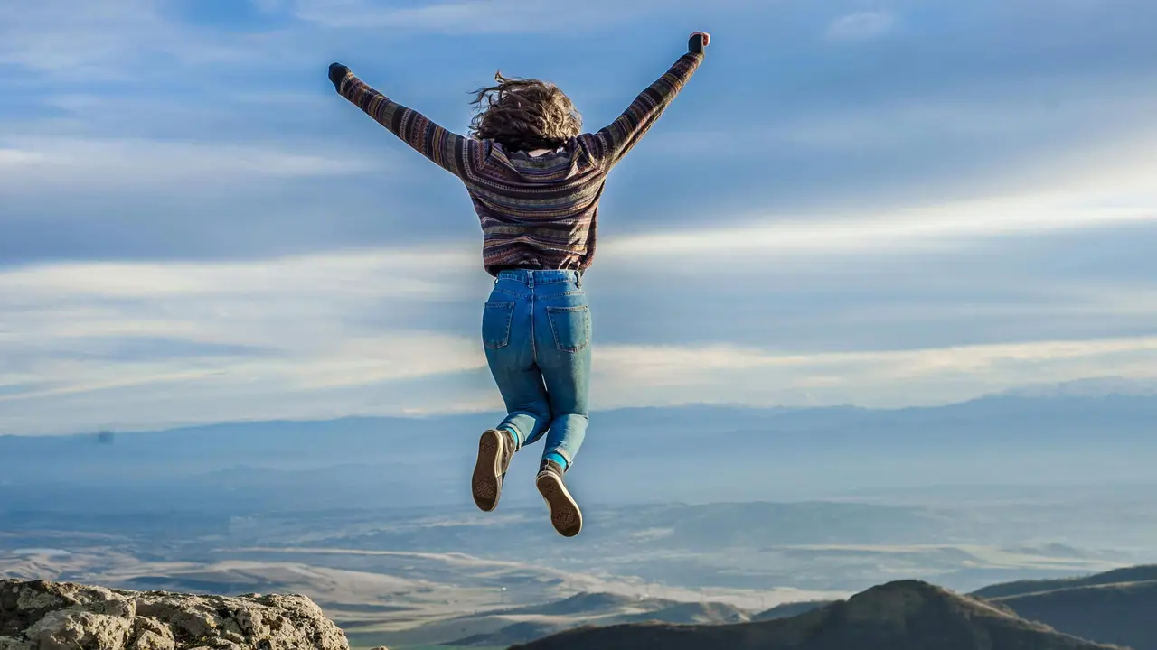 Junge Frau springt in die Luft vor Bergkulisse