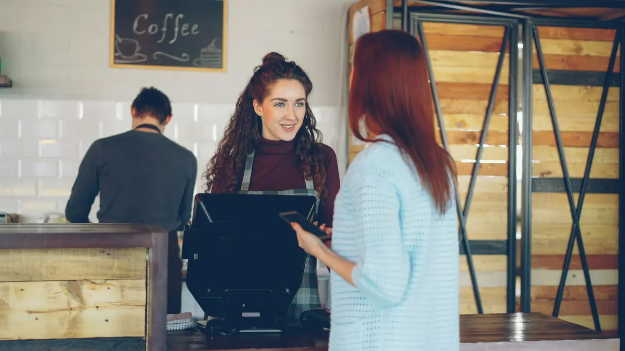 Junge Barista bedient eine Frau im Café.
