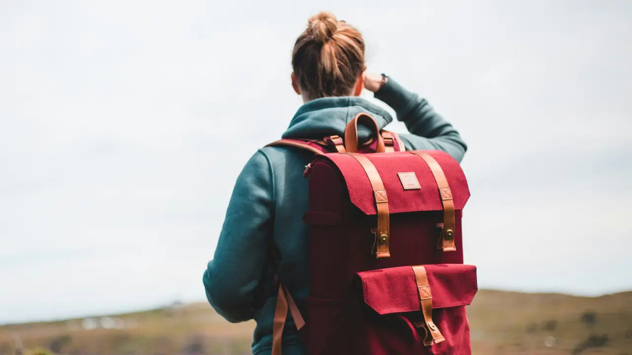 Rückenansicht einer jungen Frau mit rotem Rucksack, die in die Ferne schaut
